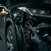 Widok z bliska na kradzież Lexusa metodą CAN Injection – złodziej w nocy wpinający emulator w magistralę CAN przez przedni reflektor auta.